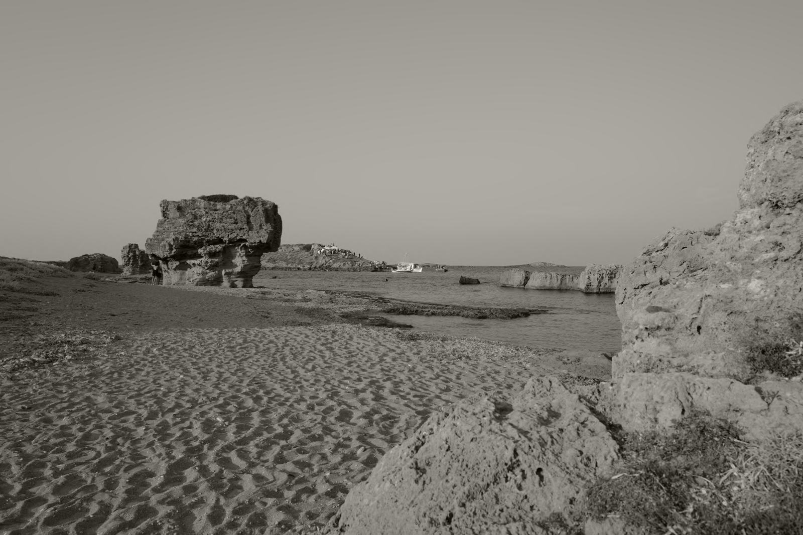 A sandy beach with a large weathered rock and a small boat