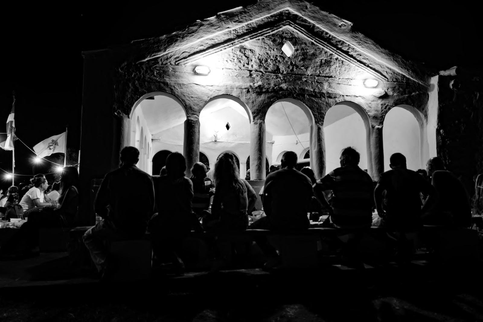 People seated at long tables in front of a lit arcade at night